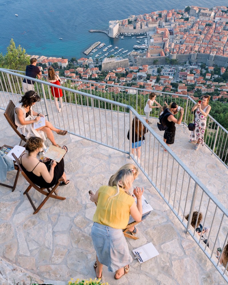 An art workshop on the terraces at golden hour, the Old Town and harbour far below.