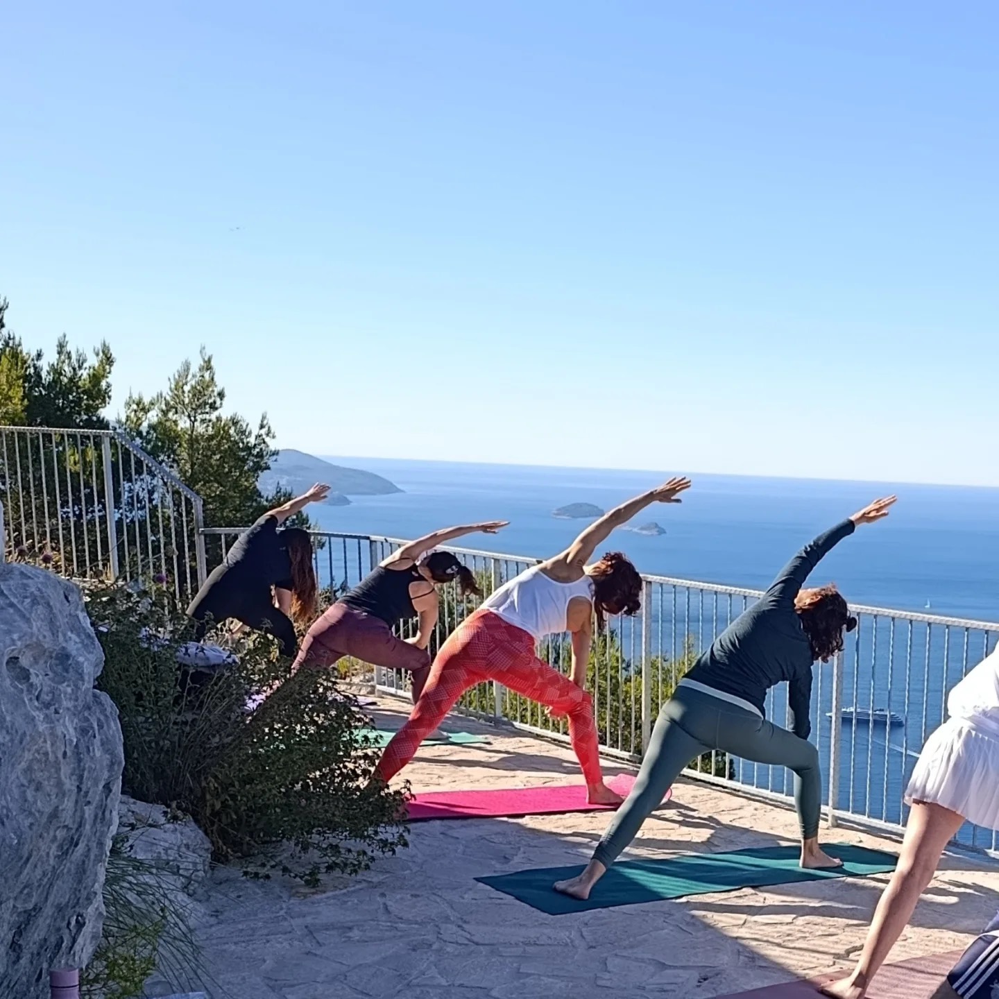 A morning yoga class on the stone terrace, the sea and islands behind them.